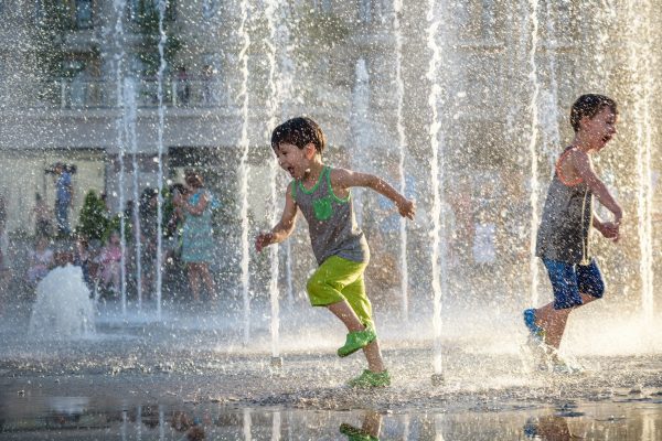 Happy kids have fun playing in city water fountain on hot summer day. Boys happy and smiling brother best friends. Ecology concept.